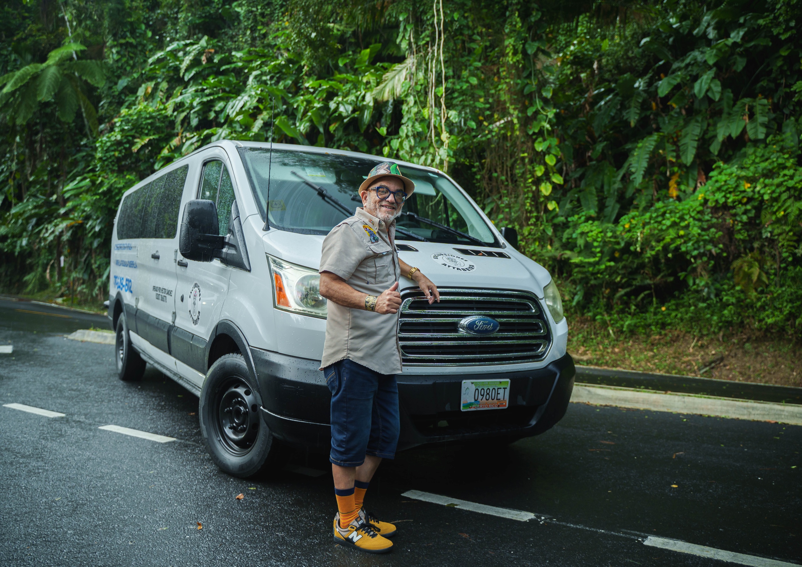 Man posing next to a van in a lush, green forest setting.