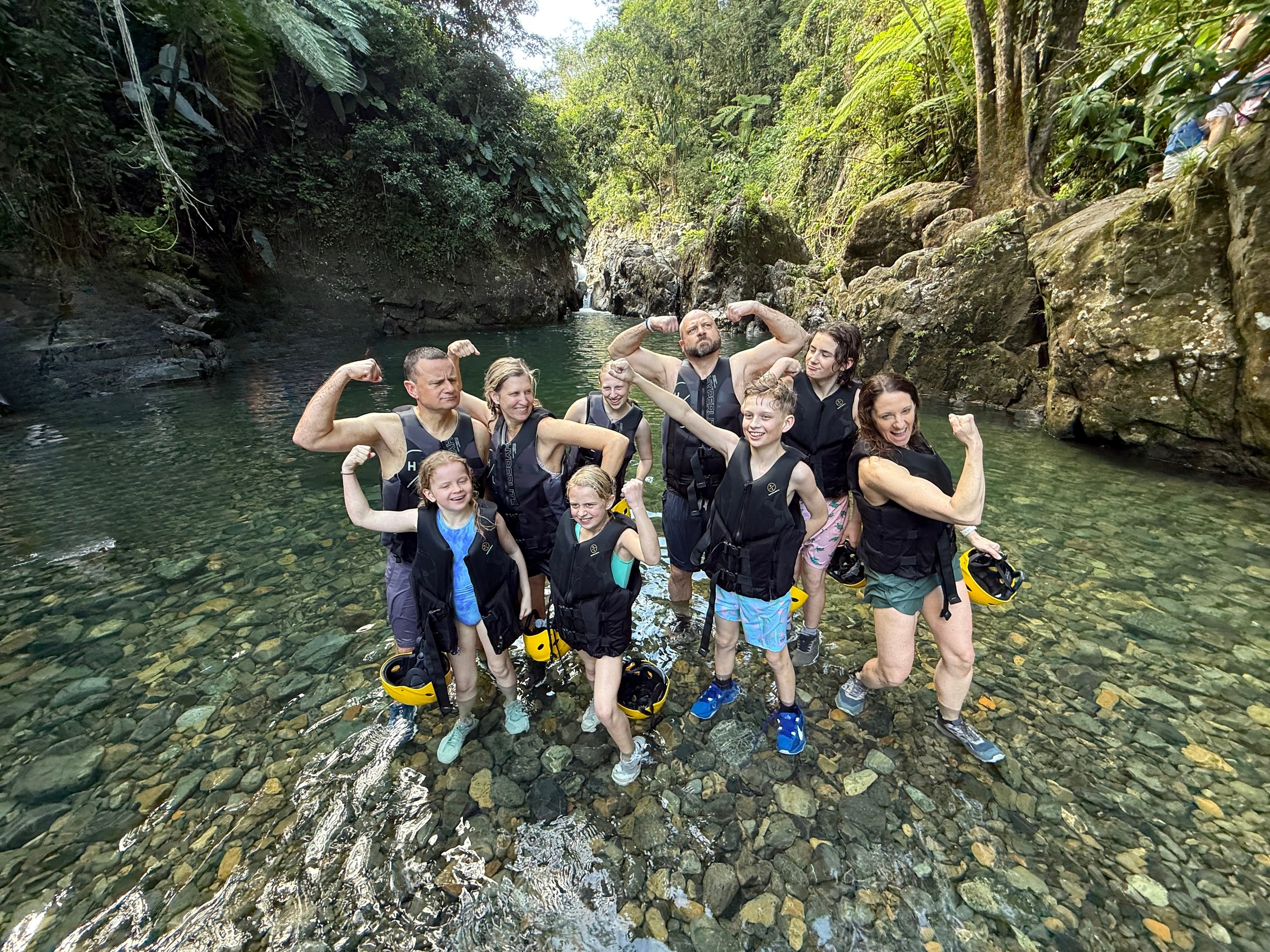 Group in life jackets posing confidently by a rocky river.