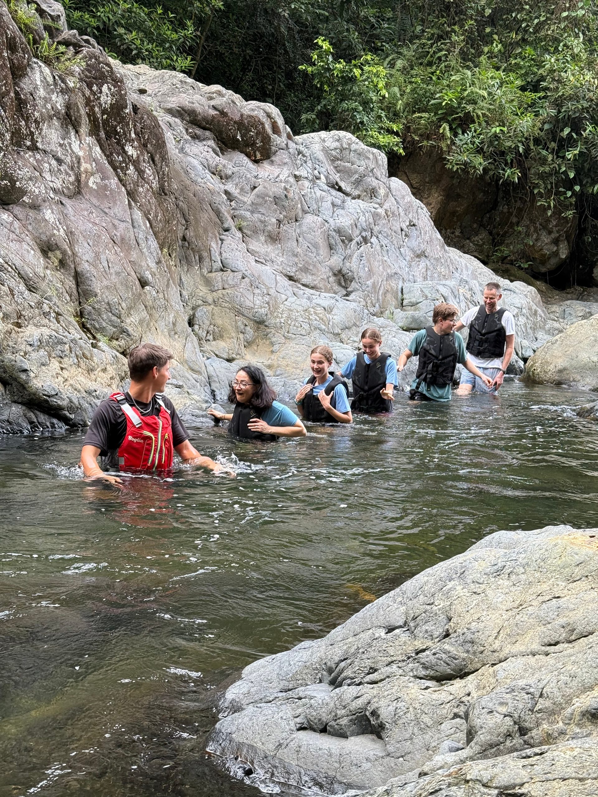 Group of people wading through a rocky stream in an outdoor setting.