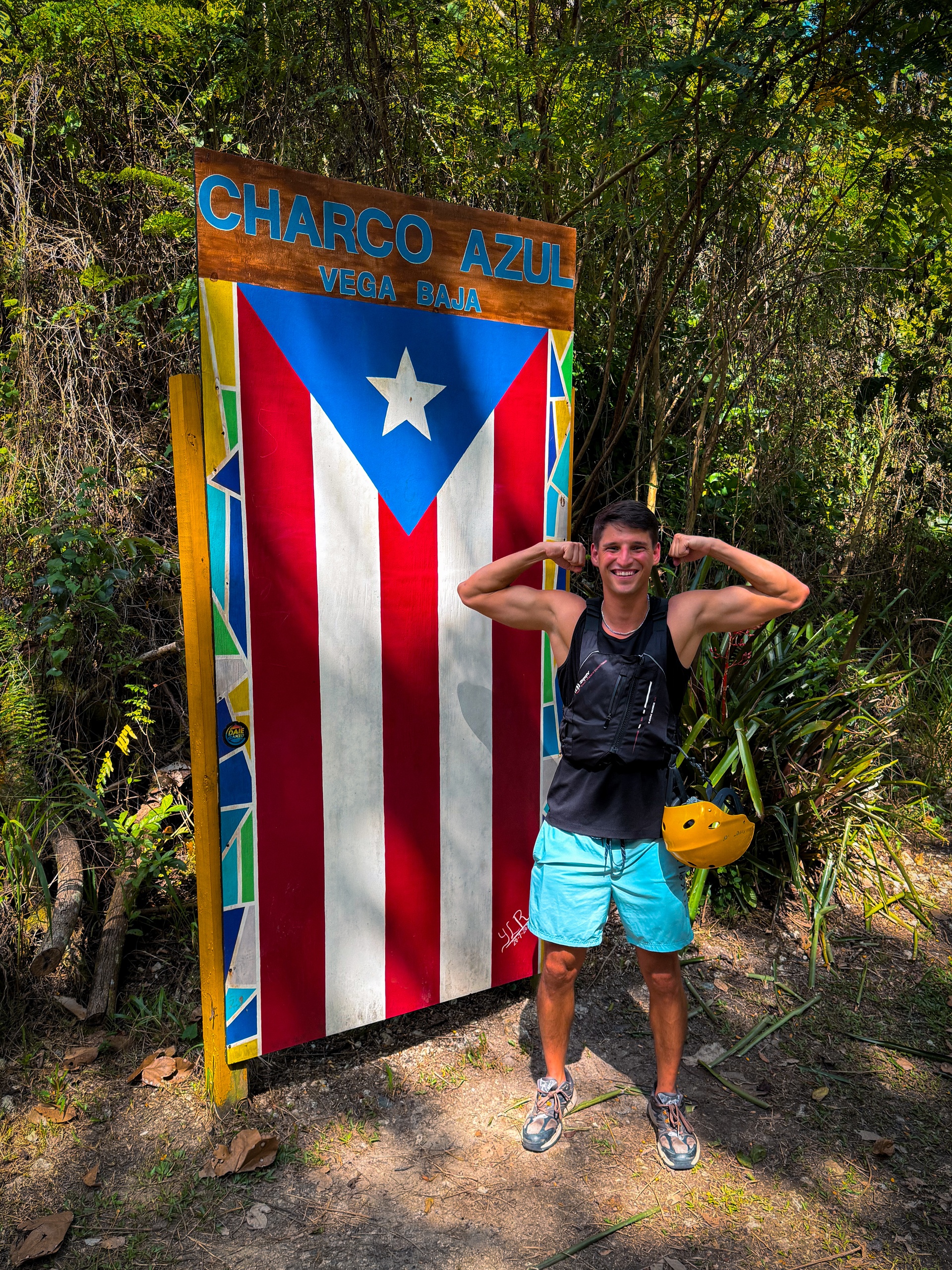 Person flexing in front of a colorful sign for Charco Azul, Vega Baja.