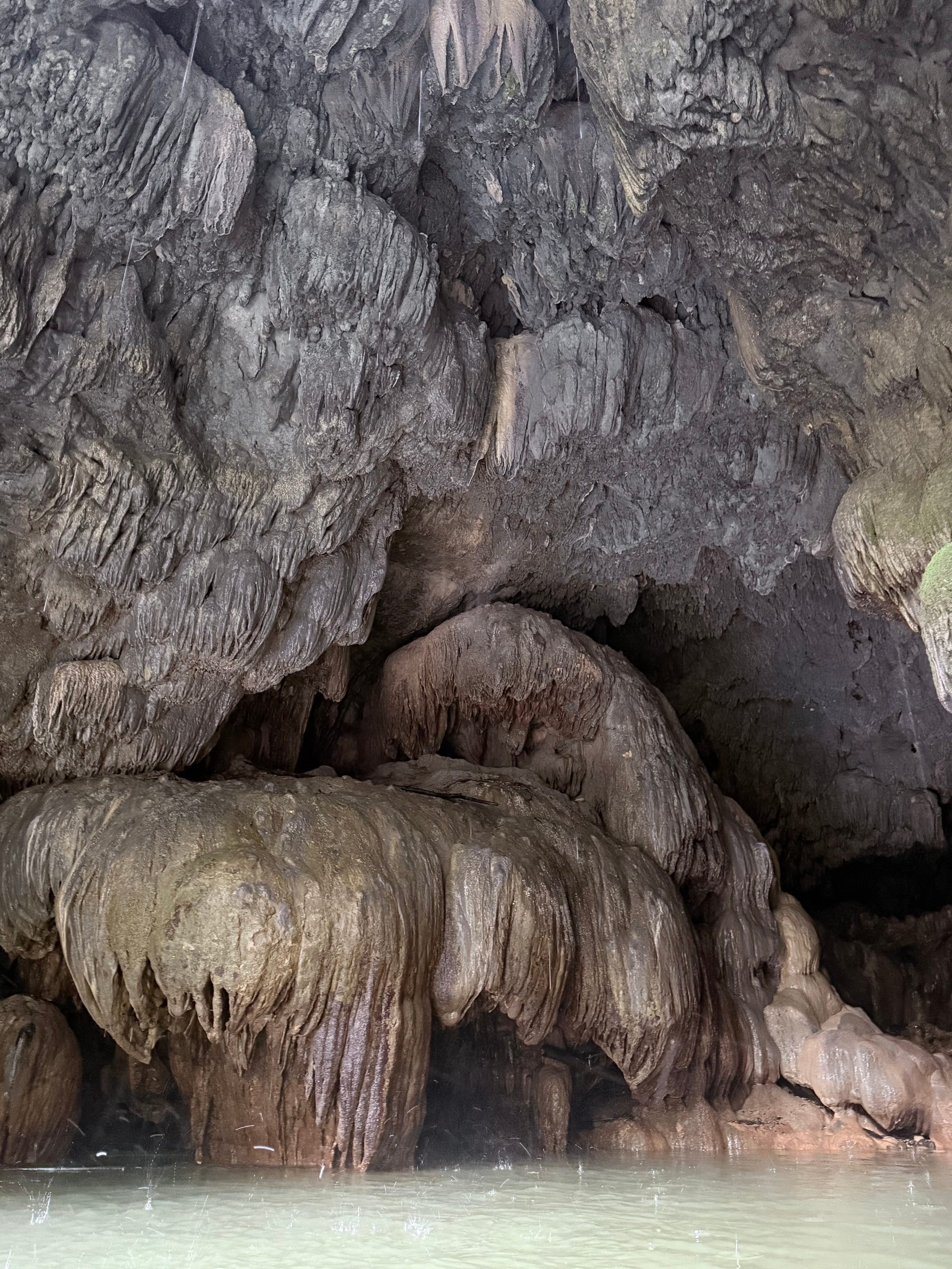 Cave interior with stalactites above and stalagmites rising from water below.