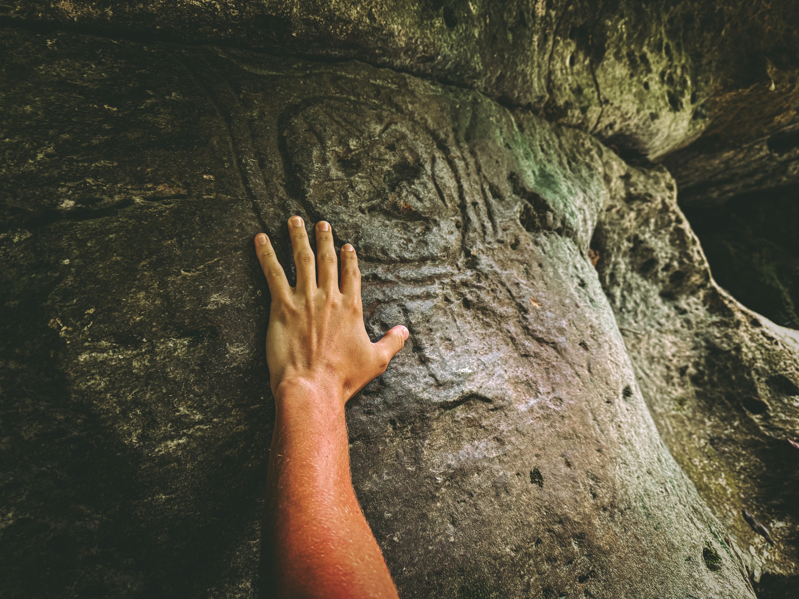 Hand touching ancient rock carving on a stone surface.
