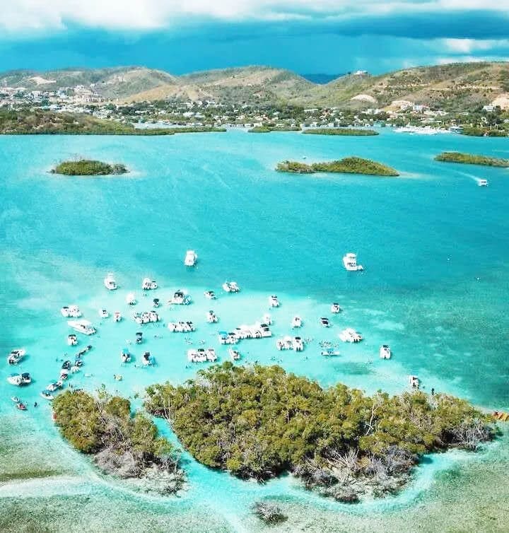 Aerial view of boats on a turquoise bay, with small islands and a coastal town in the background.