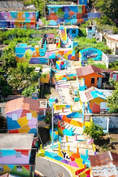 Colorful hillside houses with geometric murals and vibrant stairs in urban area.