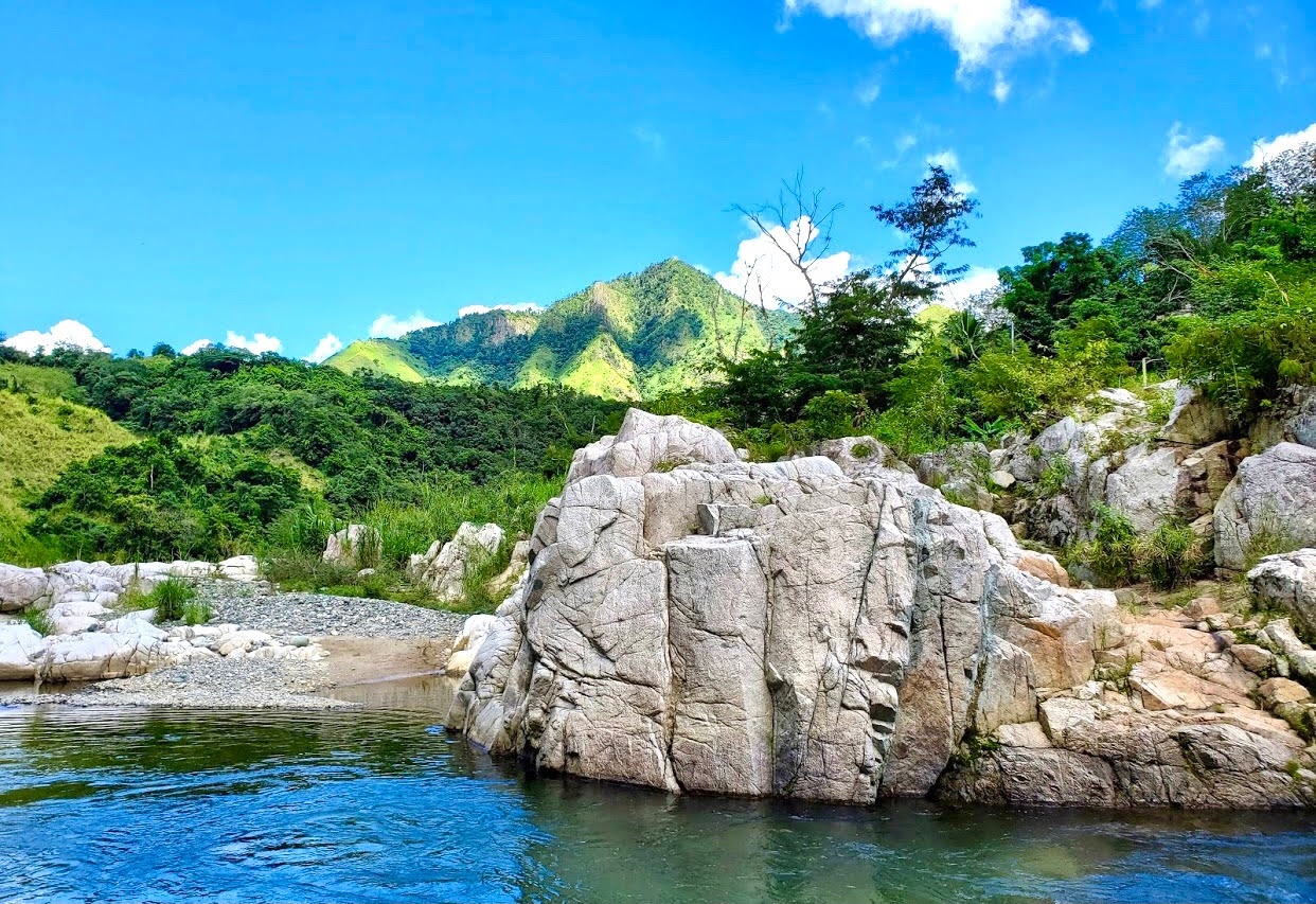 Scenic river with rocky shore and green hills under blue sky.