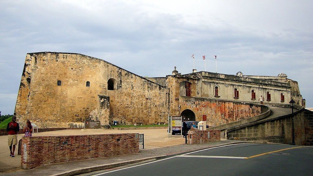Historic stone fortress with flags and arched entrance on a cloudy day.