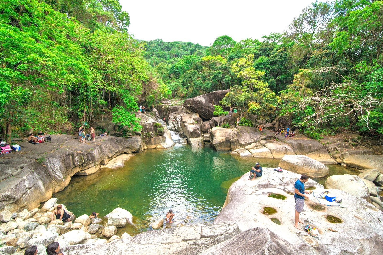 People gathered around a natural pool in a rocky, lush forest area.