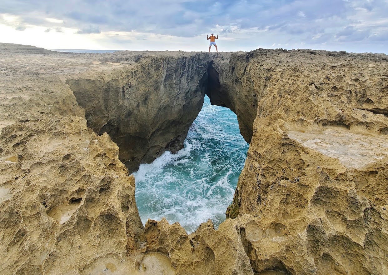 Person standing on rocky arch over ocean waves.
