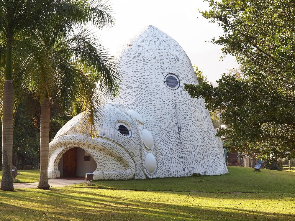 Fish-shaped white building with palm trees and grass.