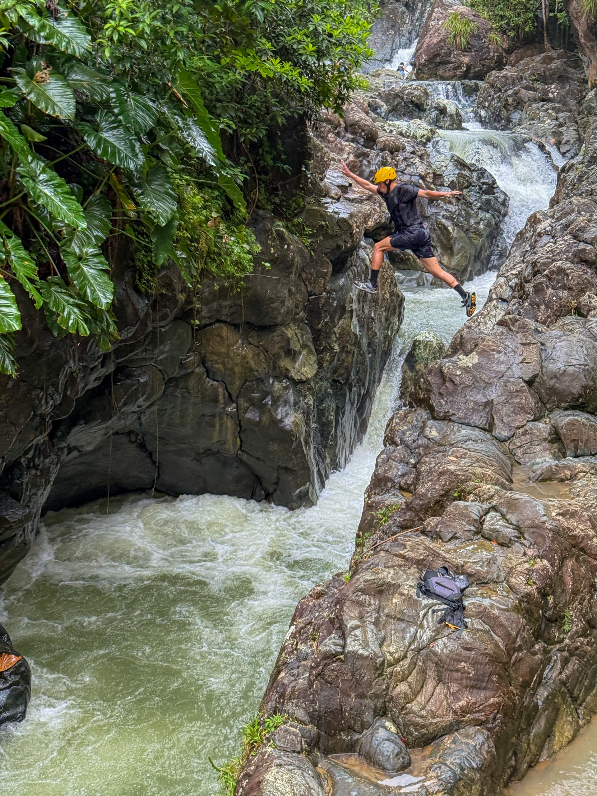 Person in helmet jumping over rocky river gorge.